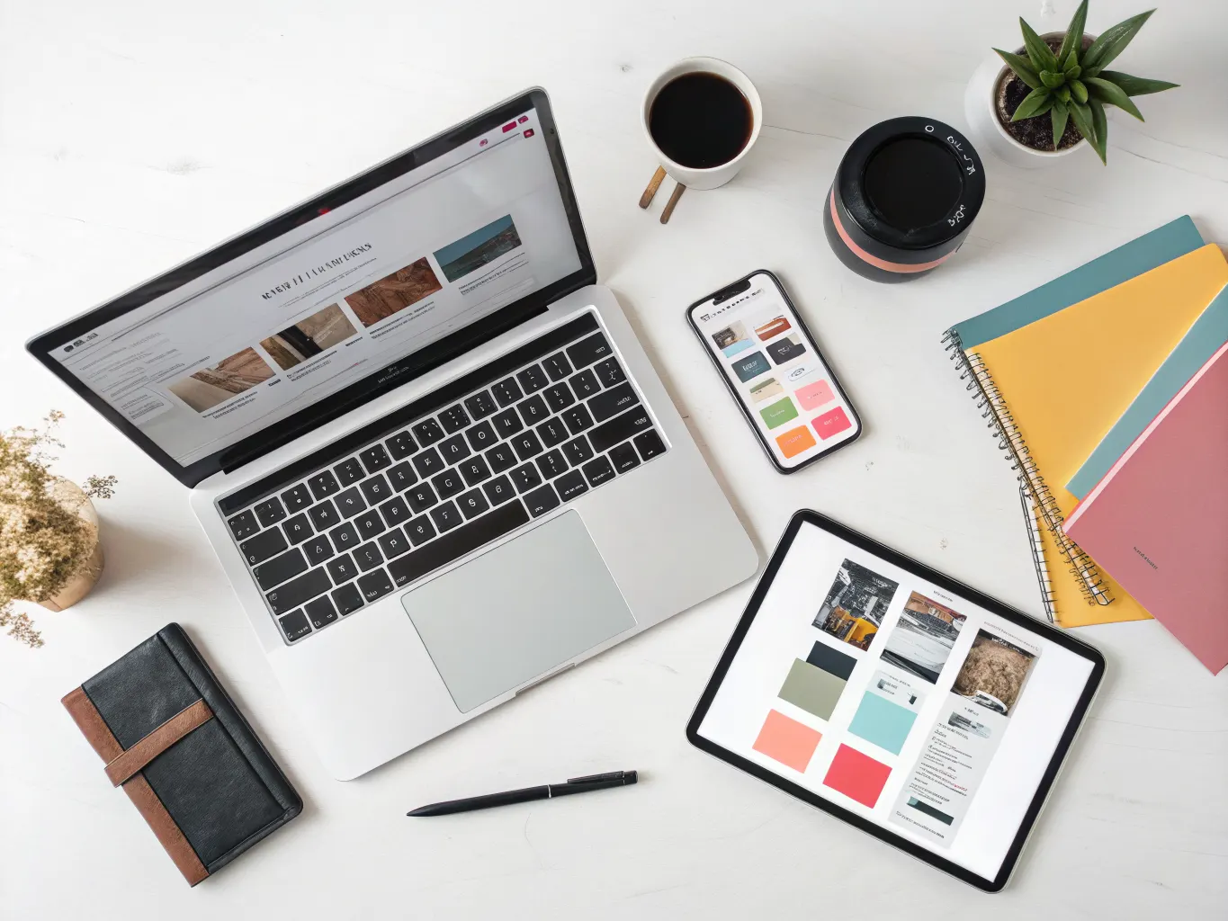 Overhead flat-lay of laptop, tablet, and smartphone showing the same website across different screen sizes with color swatches and notebooks