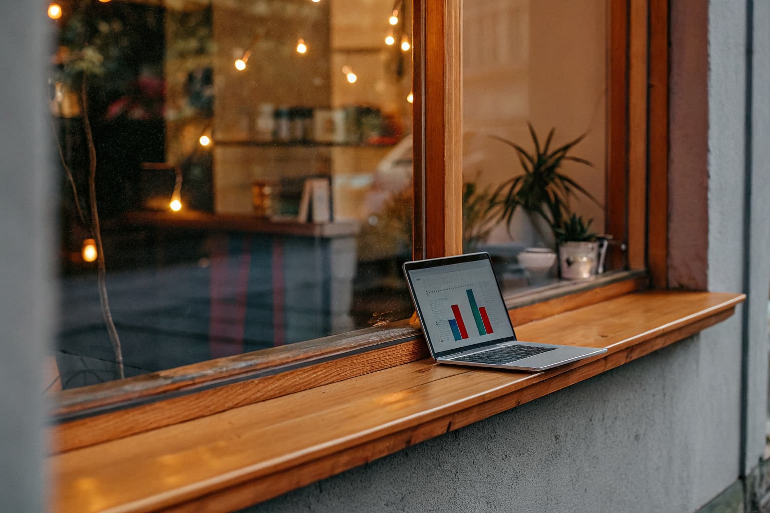 Laptop displaying a colorful growth chart resting on a wooden windowsill of a warmly lit small-business storefront at golden hour