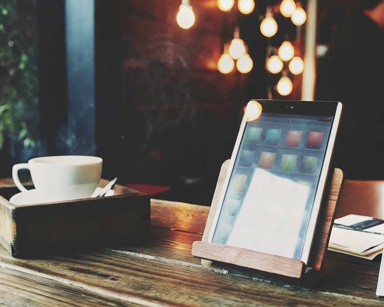 Cozy restaurant table with a tablet displaying a colorful app interface beside a steaming coffee cup and warm pendant lighting